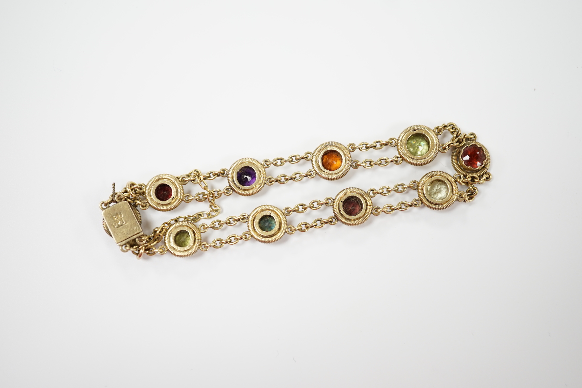 An early 20th century yellow metal (stamped 15 and also 9??) and ten stone multi gem set chain link bracelet, 16cm, gross weight 14.6 grams, the stones include amethyst, hessonite garnet and tourmaline.